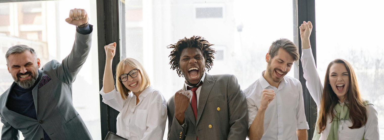Fünf Personen in Businesskleidung stehen vor großen Fenstern, heben die Fäuste und zeigen eine energische Haltung.